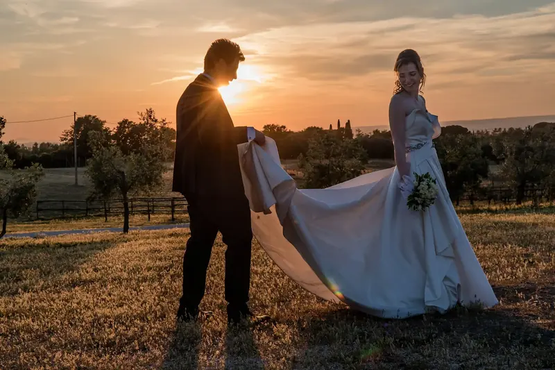 Lo sposo tiene lo strascico della sposa al tramonto tra gli ulivi